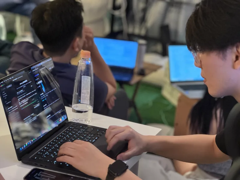 學員近距離操作筆電,螢幕顯示 AI IDE 的深色編輯介面
